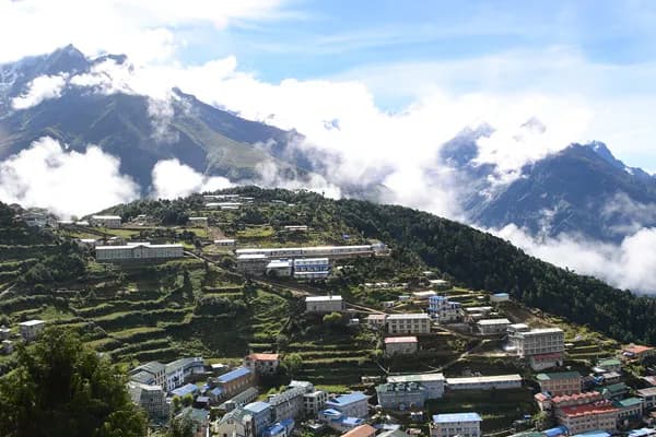 An aerial view of the terraced mountain village of Namche Bazaar with colorful teahouses built into the hillside under clouds