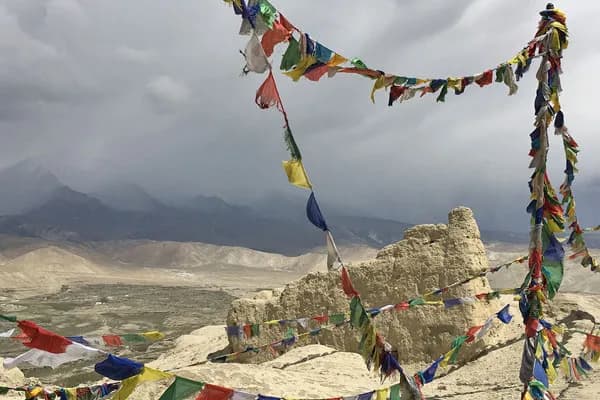 Buddhist prayer flags strung across earthen ancient ruins overlooking the arid valley of Upper Mustang under overcast skies