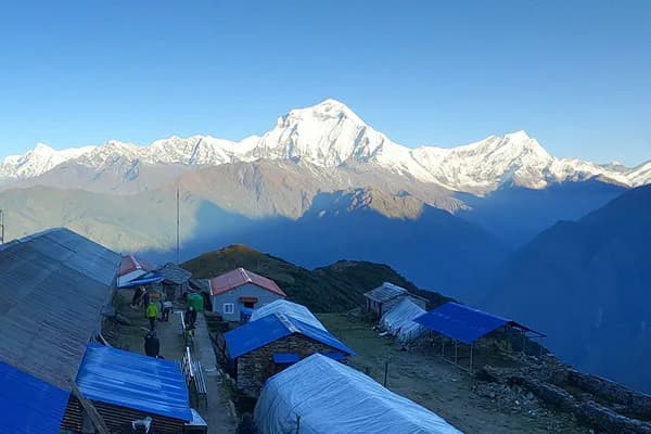 A high-altitude village settlement with blue-roofed teahouses on a ridge looking out at the snow-capped Dhaulagiri range