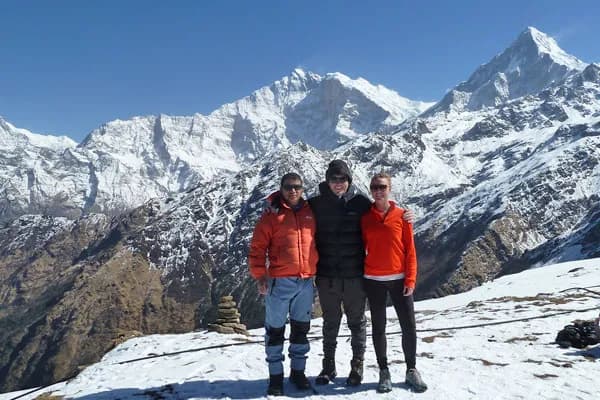 Three trekkers posing together on a snowy trail with Himalayan peaks in the background during a Nepal winter trek.