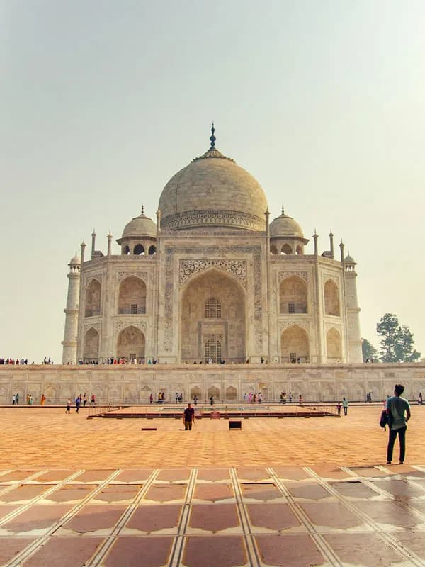 Vertical shot of tourists admiring the iconic white marble dome of the Taj Mahal in Agra, India.