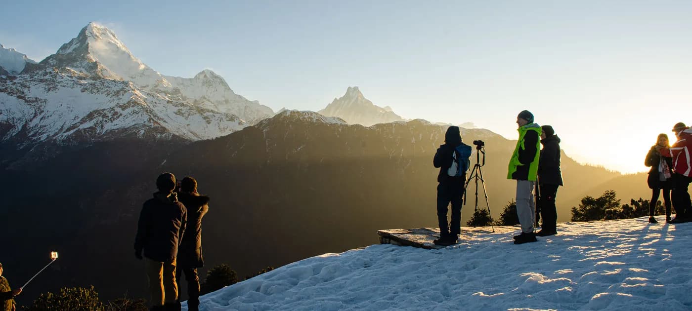 Group of tourists and photographers watching sunrise over the Annapurna mountain range from a snowy viewpoint during a short trek in Nepal