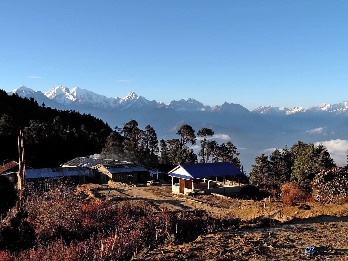 Mountain teahouse settlement at Cholangpaty with a panoramic backdrop of the snow-capped Himalayan range under a clear blue sky.