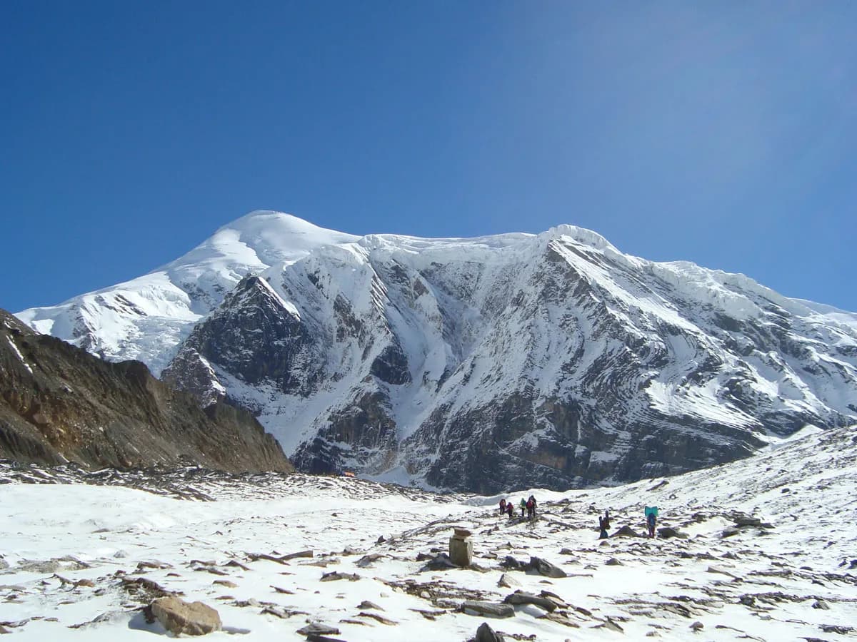 Trekkers walking across a vast, snow-covered mountain basin towards a towering white peak