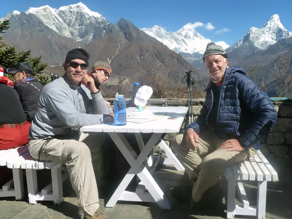 Trekkers enjoying a meal on a sunlit terrace with views of Mt. Everest, Lhotse, and Ama Dablam