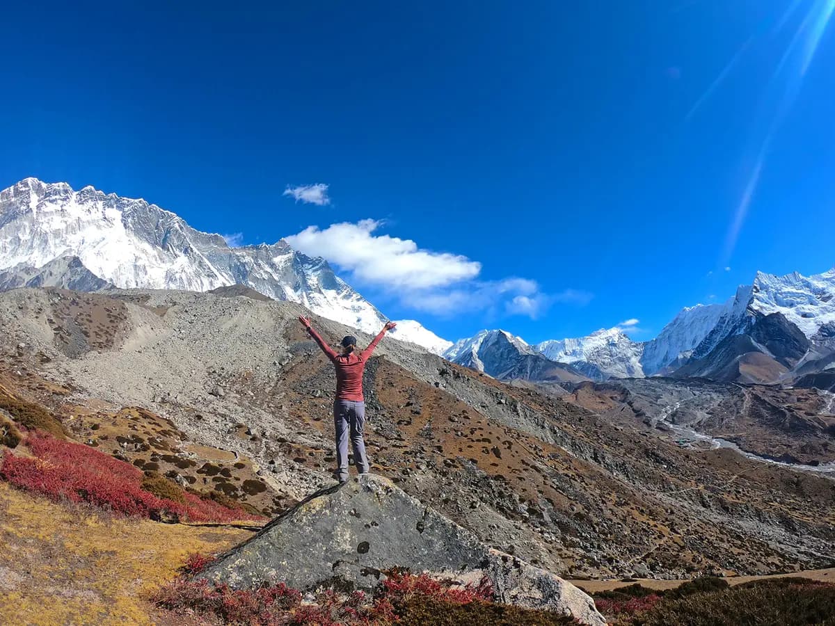 Trekker with open arms standing on a rock overlooking Lhotse and Himalayan valleys.