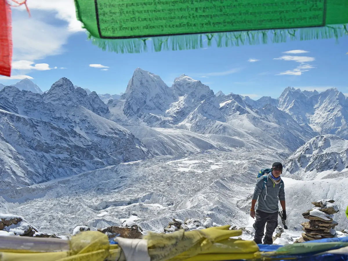 Hiker looking at snow-capped Himalayan peaks framed by prayer flags on the Everest Base Camp via Gokyo Lakes trek