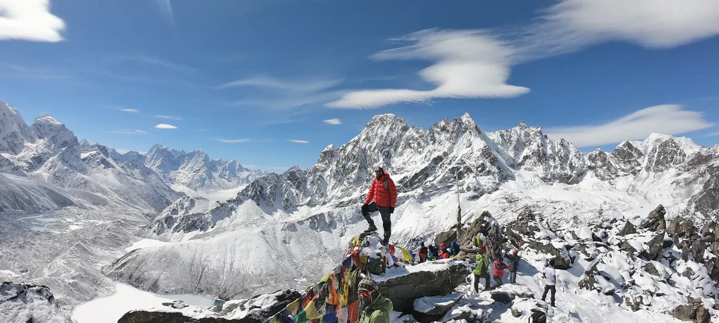 Hiker standing on a prayer-flag adorned peak overlooking Gokyo lakes and snow-capped mountain ranges