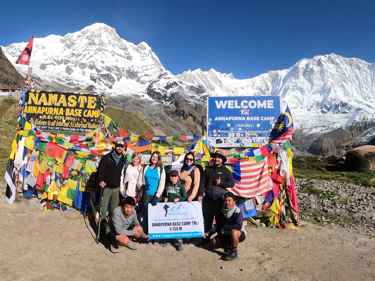 Group of happy trekkers posing with a Rugged Trails Nepal banner at the Annapurna Base Camp signpost