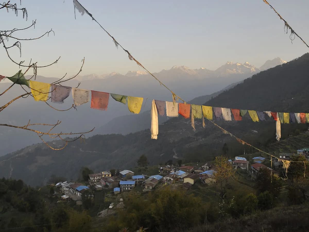 Traditional Himalayan village in the Helambu Valley framed by colorful prayer flags and snow-capped mountain peaks.