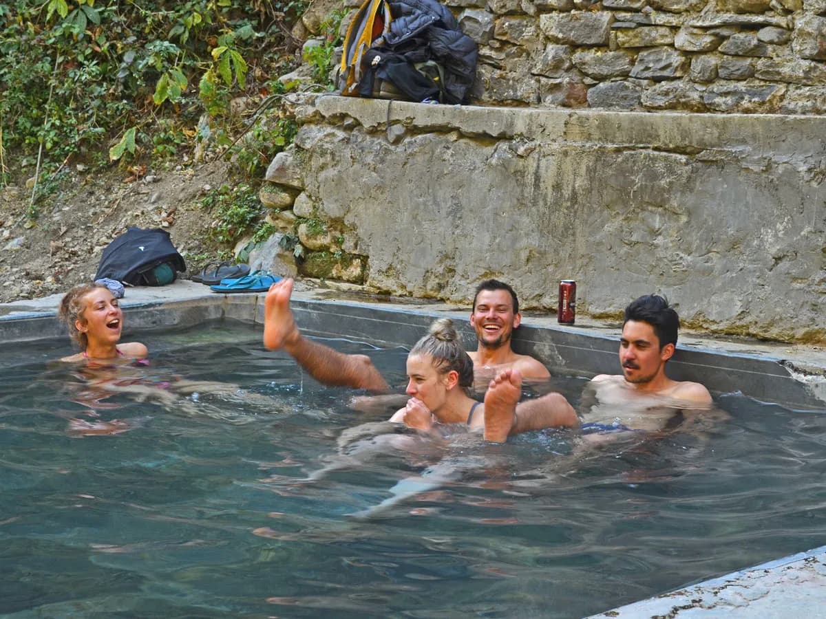 A group of tourists sitting, relaxing, and laughing in the outdoor natural hot spring pool at Jhinu Danda.