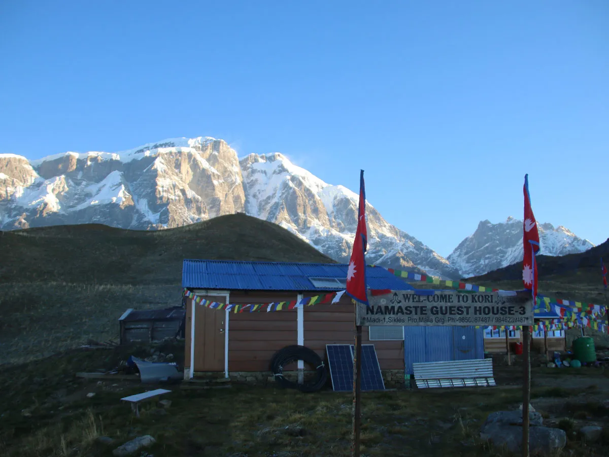 Namaste Guest House sign with prayer flags and snow-capped Himalayan mountains at Kori Danda, Nepal