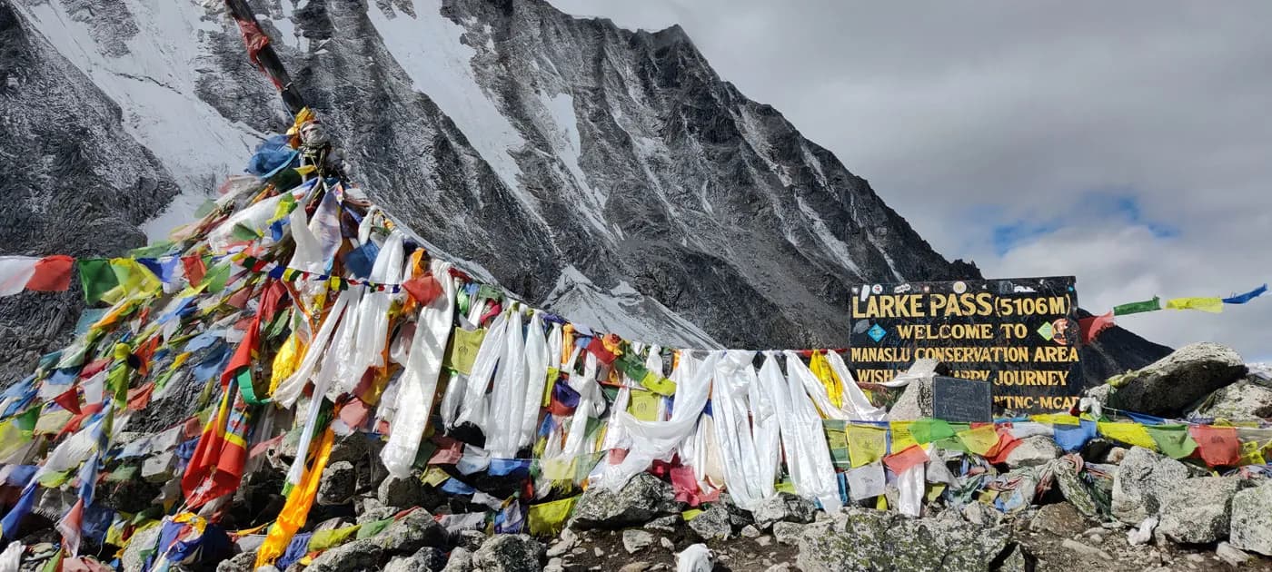 Landmark sign for Larke Pass 5106m surrounded by colorful prayer flags on the Manaslu Circuit Trek