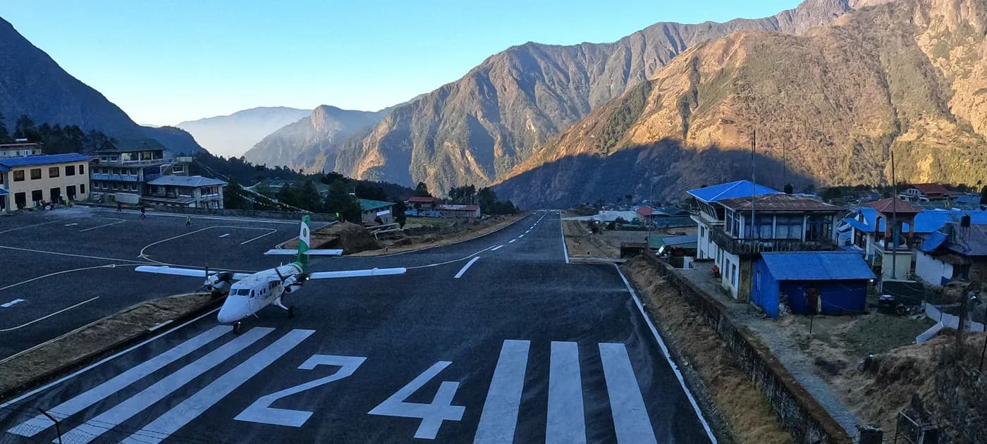 Small twin-otter aircraft parked on the short, sloped runway of Lukla Airport surrounded by steep Himalayan mountains.