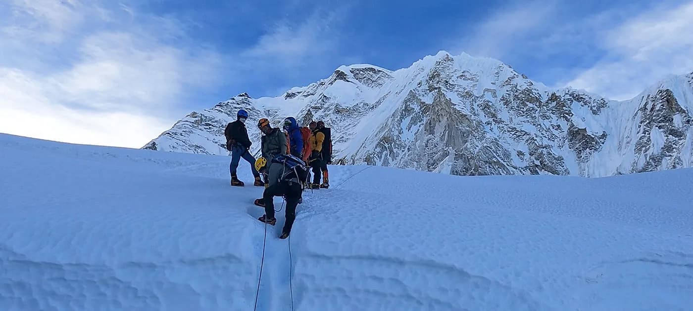 A team of mountaineers in cold-weather gear ascending a steep snow slope connected by safety ropes in the Nepal Himalayas