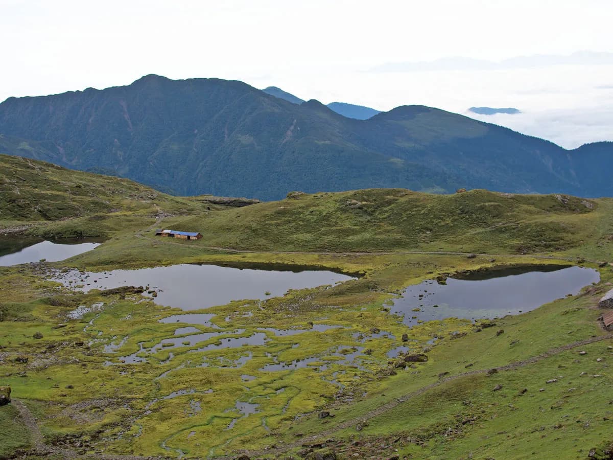 High-angle landscape view of the sacred Panch Pokhari glacial lakes surrounded by green meadows and distant misty mountains.