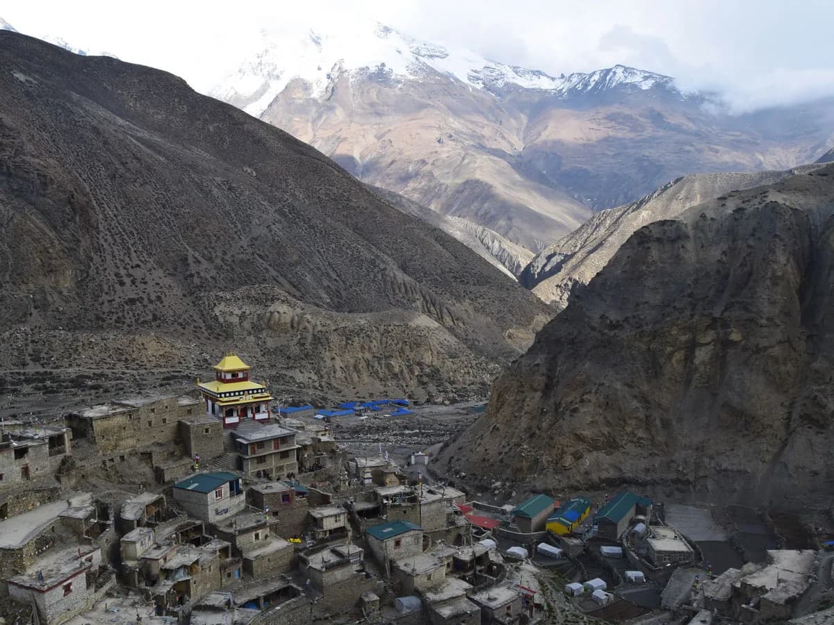 Panoramic view of Phu village nestled in a rocky canyon with traditional stone houses, a colorful monastery, and snow-capped Himalayan mountains in Nar Phu Valley, Nepal.