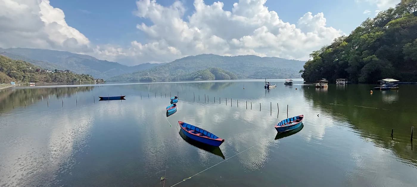 Brightly painted wooden boats floating on the calm, reflective waters of Phewa Lake surrounded by forested hills