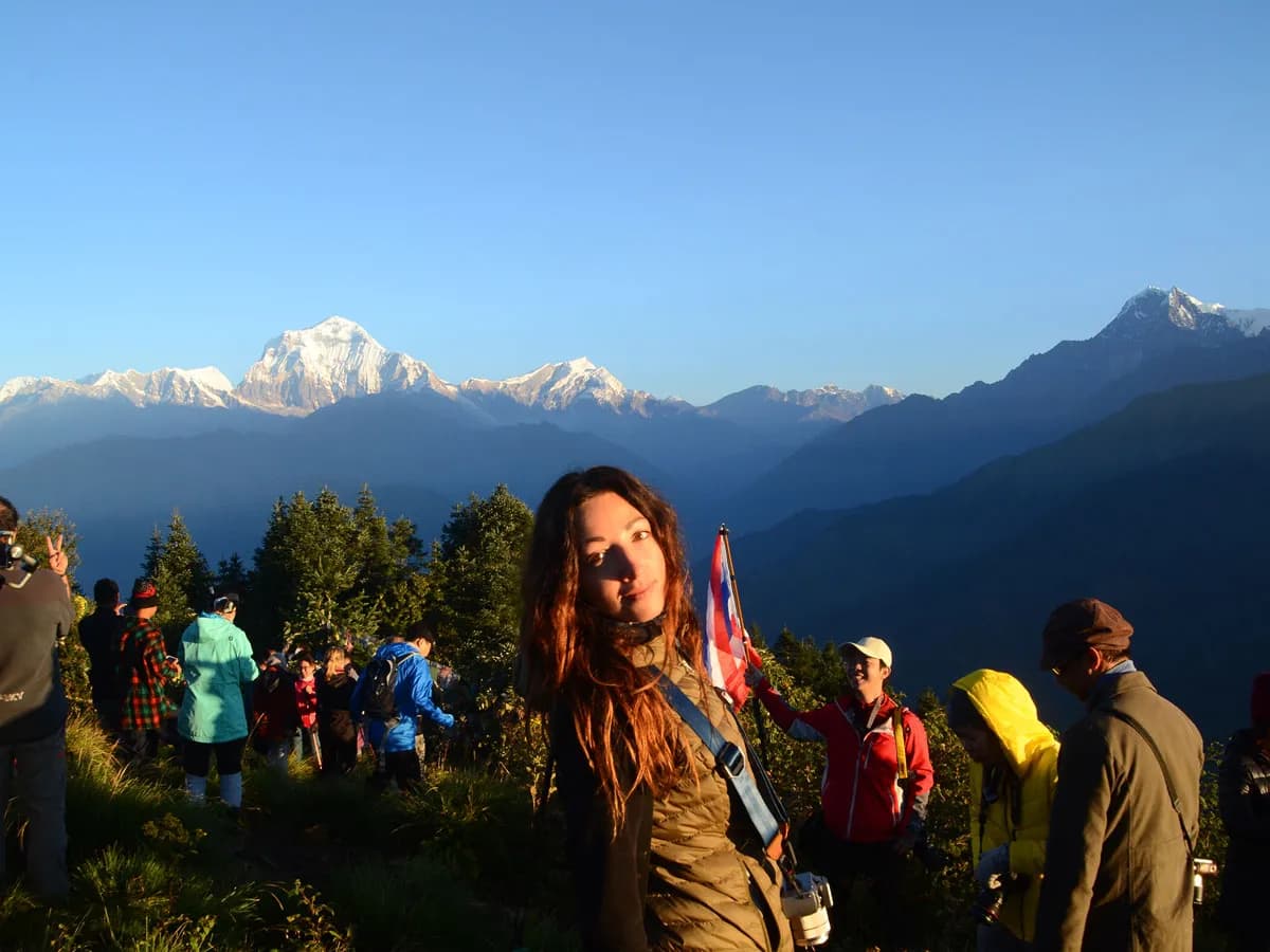 Female trekker posing at Poon Hill viewpoint with Dhaulagiri and Annapurna range at sunrise