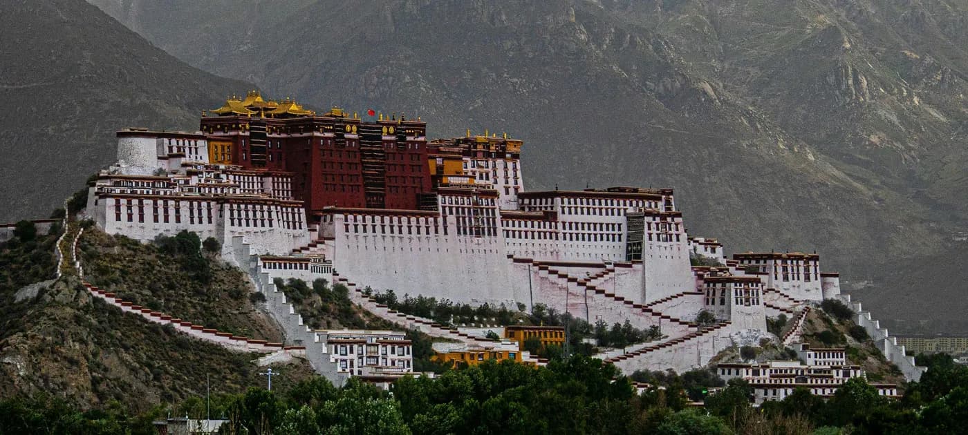 Panoramic view of the grand Potala Palace set against the rugged Himalayan mountain backdrop in Lhasa, Tibet.