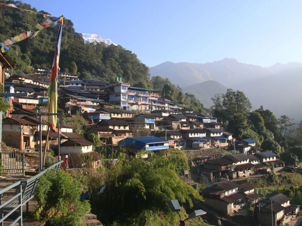 Traditional Gurung village of Sikles built on a hillside with prayer flags and mountains in the distance.