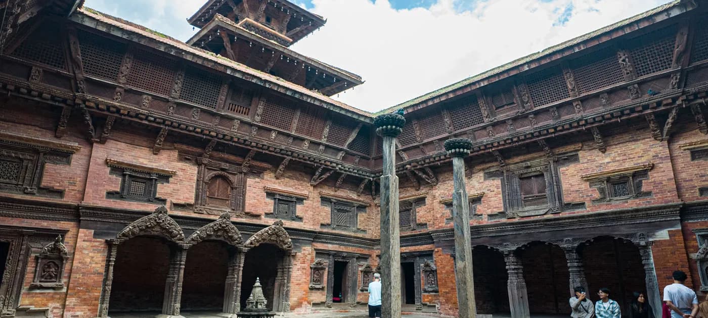 Intricately carved wooden windows and stone courtyard surrounding the Tusha Hiti sunken royal bath at Sundari Chowk in Patan Durbar Square