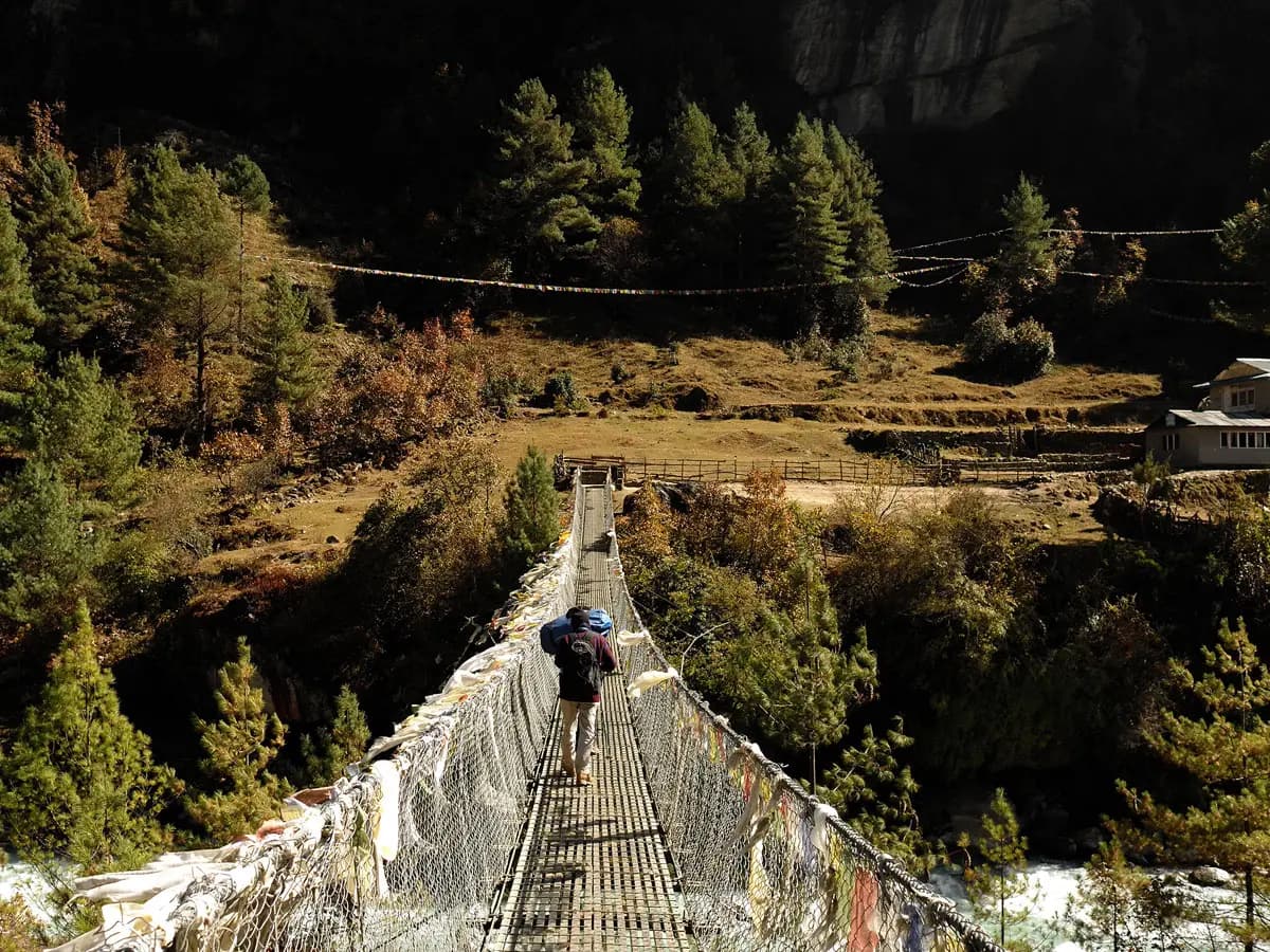Trekker crossing a long suspension bridge adorned with prayer flags.