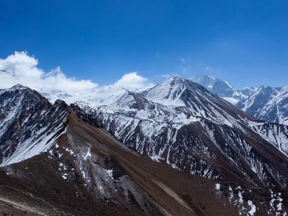 Panoramic view of snow-capped Himalayan mountain ridges and rugged high-altitude valleys under a clear blue sky in the Langtang region.