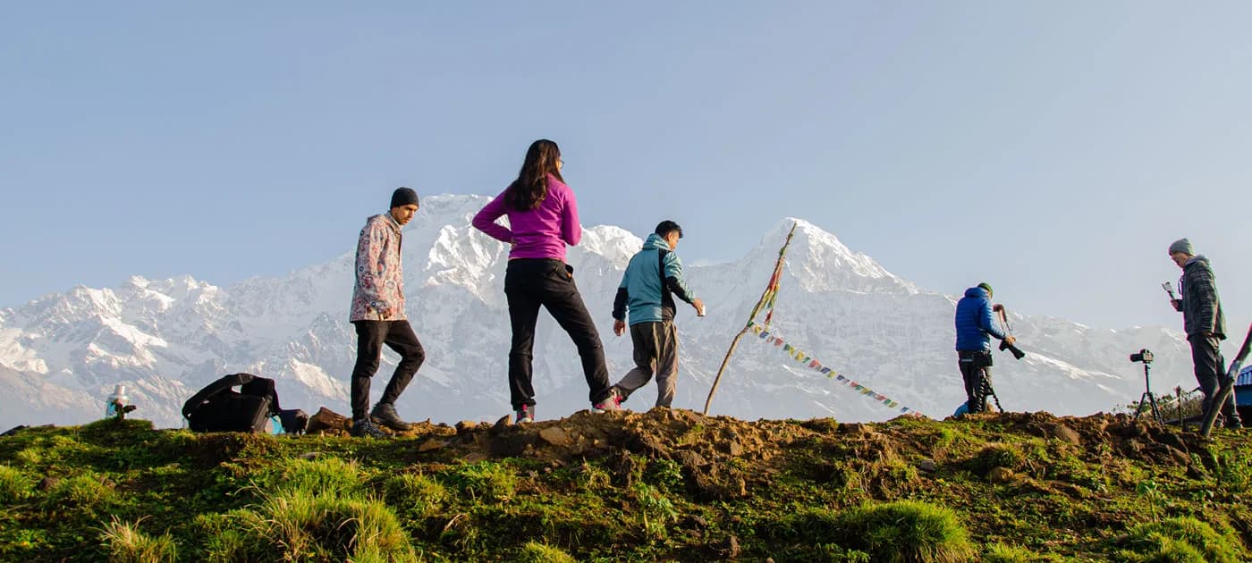 Group of trekkers standing on a grassy ridge admiring the snow-capped Himalayan mountain range under a clear sky in Nepal