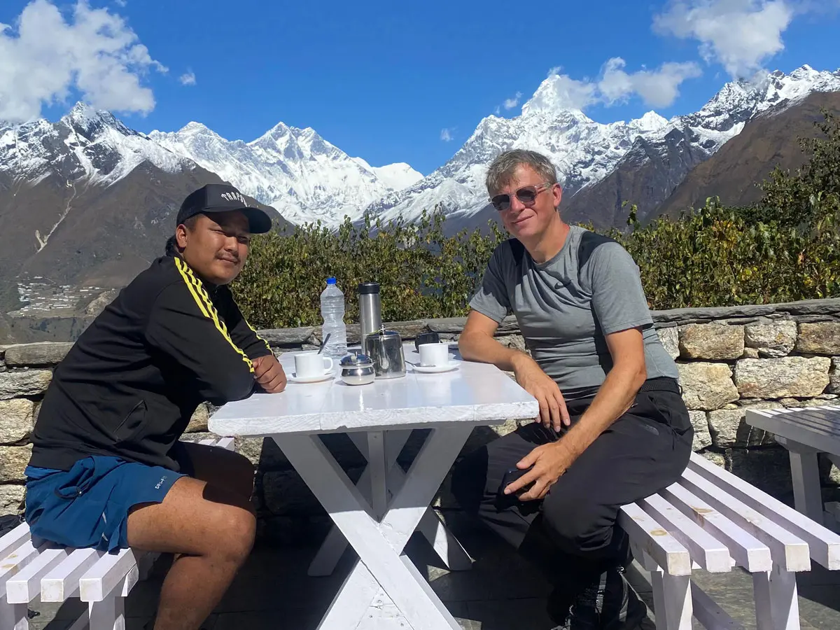 Trekkers sitting outdoors with tea overlooking snowy Himalayan peaks