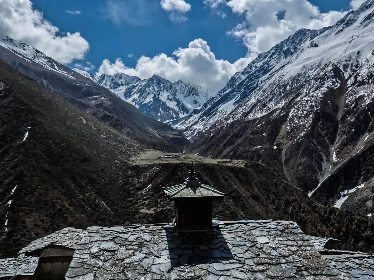 Slate tile roof with a central stupa spire overlooking a vast Himalayan valley and snow-covered mountain peaks under a blue sky