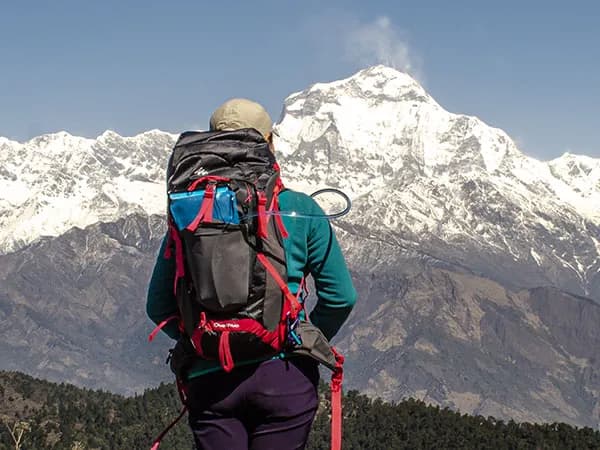 Rear view of a trekker carrying a Quechua backpack looking out at snow-capped Himalayan peaks on the Annapurna Foothills Circuit Trek in Nepal.
