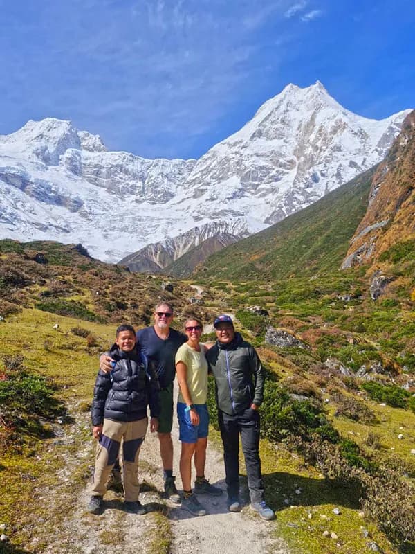 Trekkers and local guides smiling together on a sunny trail with snowy mountain peaks in the background during the Manaslu Circuit trek