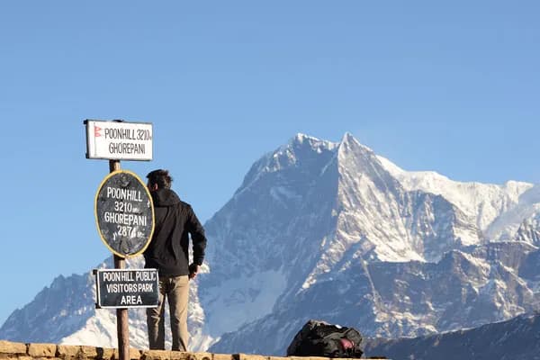 A trekker standing next to the Poon Hill 3210m elevation signpost looking out at Mount Machhapuchhre in the Annapurna range