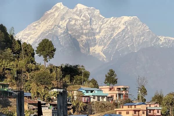 A hillside village with traditional colorful homes set beneath the massive snow-capped peak of Mount Gaurishankar.