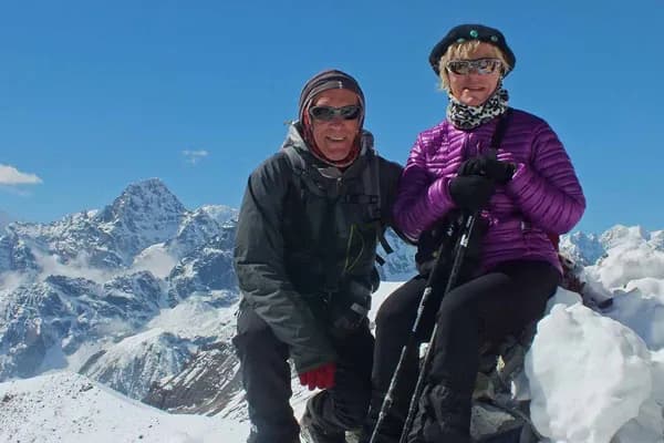 A man and woman standing together next to colorful Buddhist prayer flags on Kala Patthar viewpoint with snow-covered Himalayan peaks in the background.