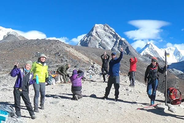 An international group of yoga trek participants and instructor practicing standing yoga poses together on an open field in front of Tengboche Monastery.