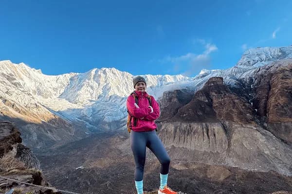 A female trekker in a pink jacket standing on a mountain ridge with massive snow-capped peaks of the Annapurna massif behind her