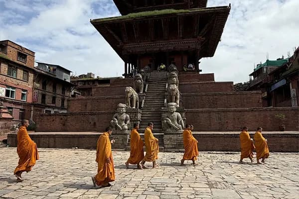 Buddhist monks wearing traditional orange robes walking across the stone-paved Taumadhi Square in front of the multi-tiered Nyatapola Temple in Bhaktapur, Nepal