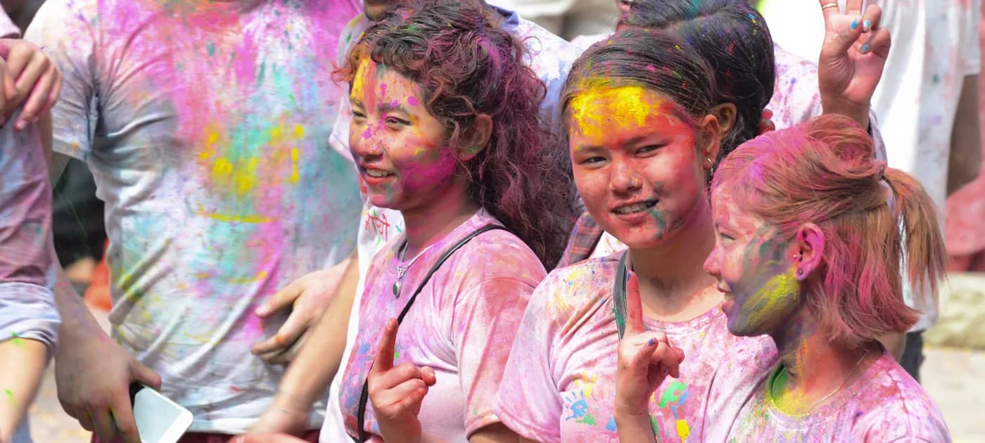 A group of happy Nepalese young women covered in bright pink, yellow, and green Holi color powder enjoying the festival.