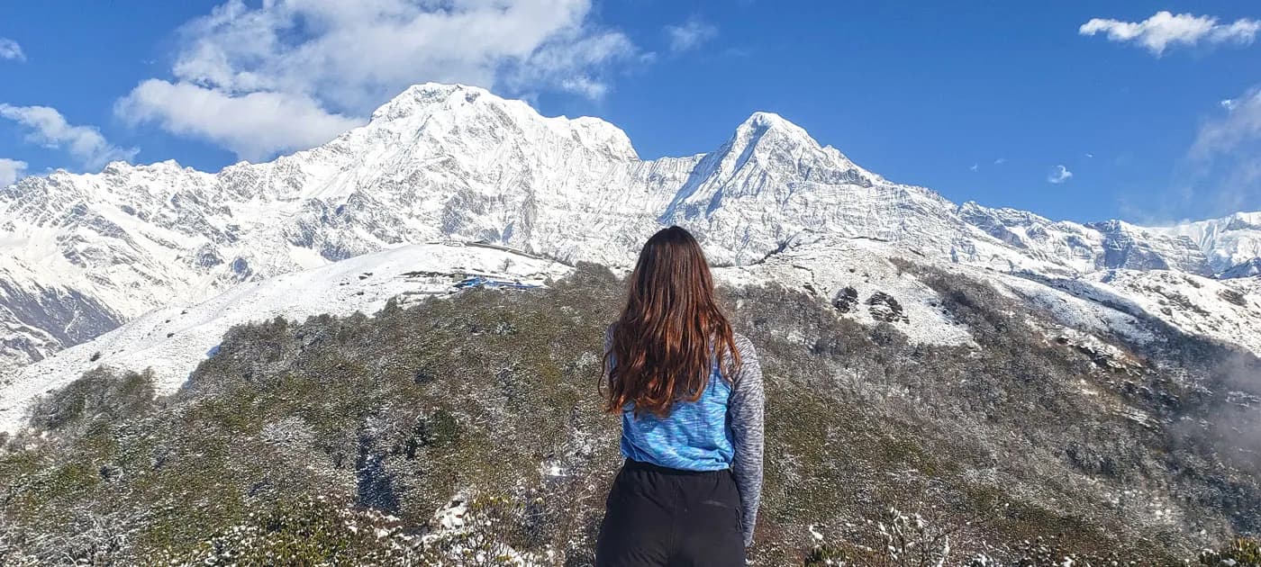 A female trekker seen from behind looking out at the snow-covered Annapurna massifs