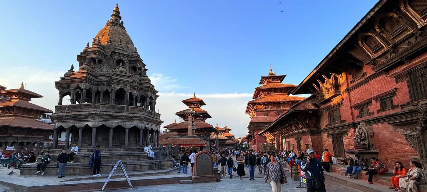 Visitors walking through Patan Durbar Square surrounded by ancient stone shikhara temples and historic brick palace architecture