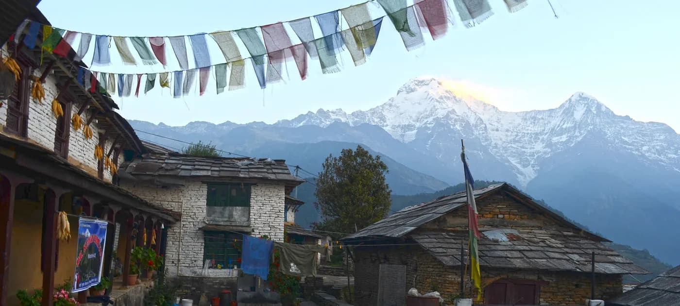 Traditional Gurung stone houses in Ghandruk village with colorful prayer flags hanging overhead against a backdrop of snow-capped mountains