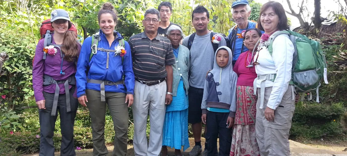 Foreign trekkers wearing flower garlands posing with local indigenous family members during a community homestay trekking trip in Nepal