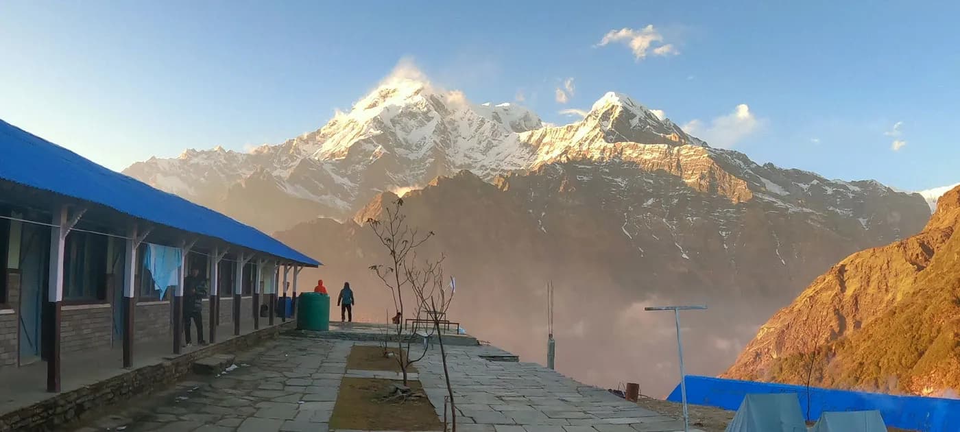 A mountain lodge balcony overlooking a dramatic panorama of snow-covered Himalayan peaks bathed in warm golden sunlight during Mardi Himal trek.