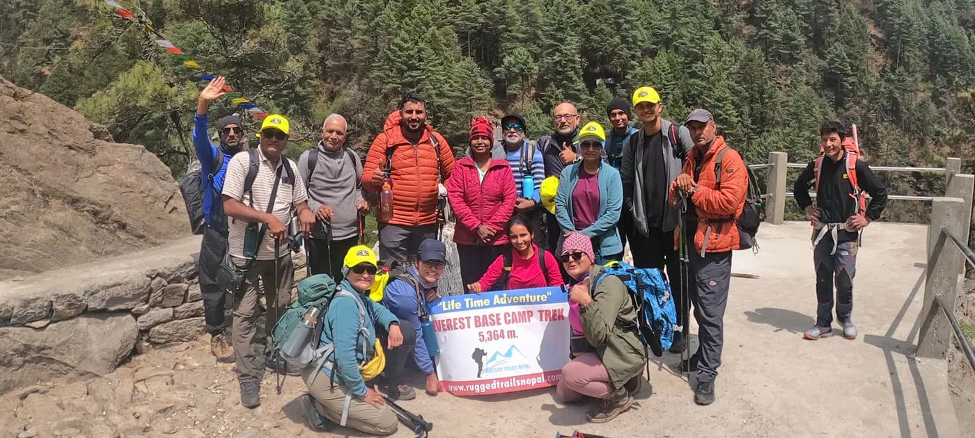 A large group of male and female trekkers holding a banner labeled Lifetime Adventure Everest Base Camp Trek along a mountain path