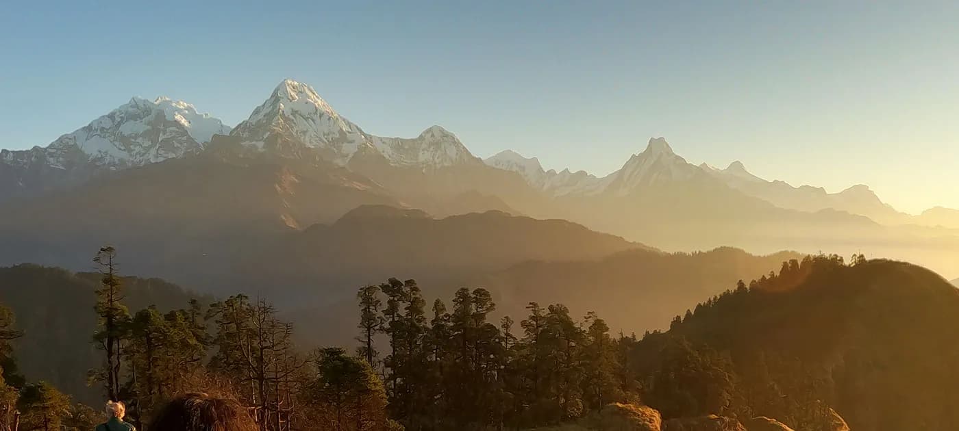 Wide panoramic landscape showing the golden morning glow over the Annapurna range and the distinct peak of Machhapuchhre.