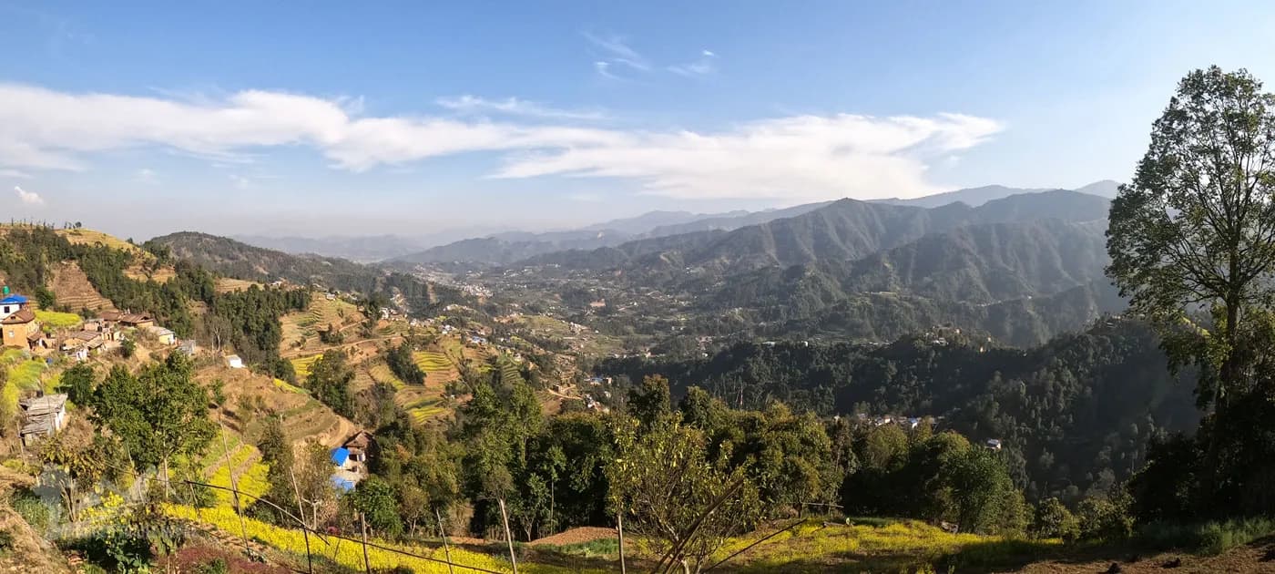 Panoramic view of green hills, mustard fields, and traditional village houses in the Nepalese countryside.