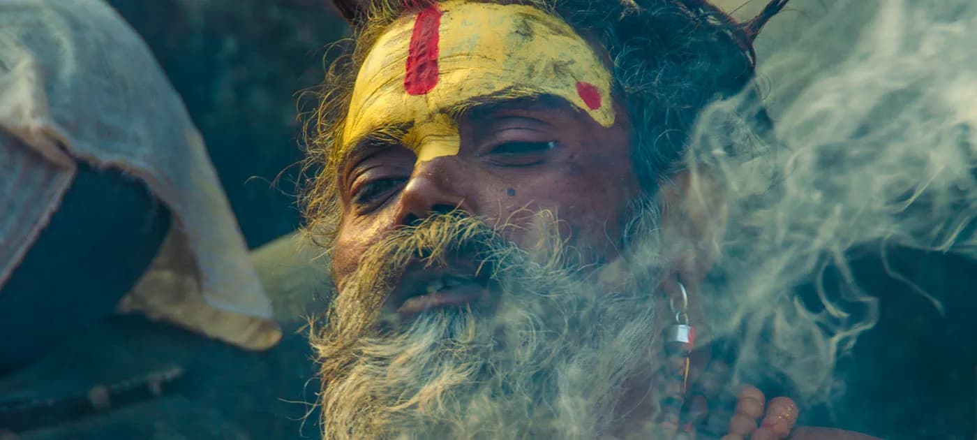 Close-up portrait of a Sadhu in Nepal with yellow and red facial paint surrounded by dense smoke at Pashupatinath Temple.