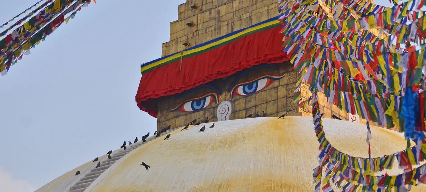 Close-up view of the Buddha eyes and colorful prayer flags on a stupa, essential for travelers planning a trip to Nepal.